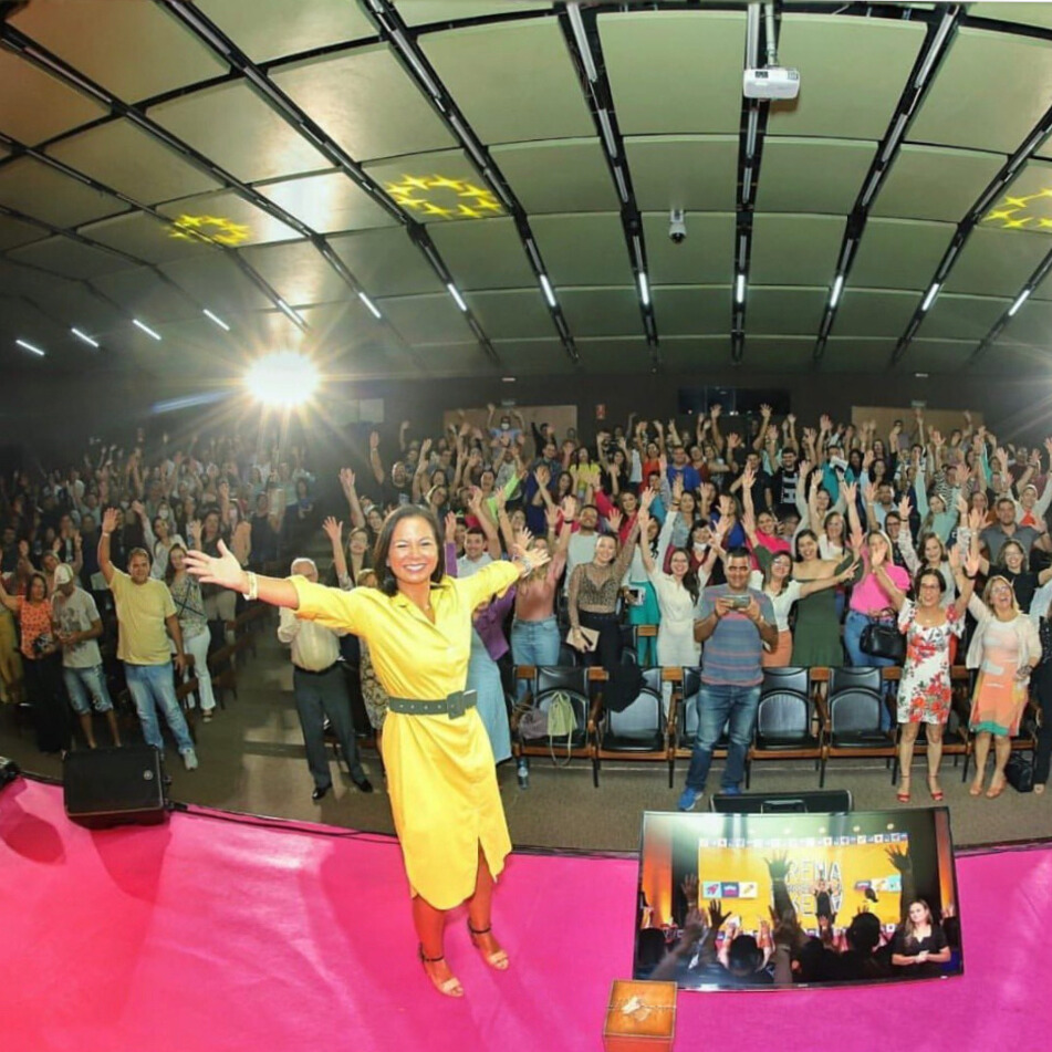 Mariana Arantes palestrando no SEBRAE com plateia de braços levantados